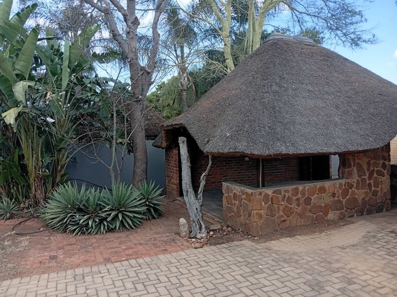 Outdoor thatched lapa area featuring stone and brick construction, set within a landscaped garden with paved surroundings.