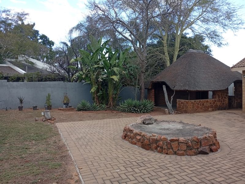 Spacious rear garden featuring a paved patio, a traditional thatched lapa, and a stone-clad fire pit area.