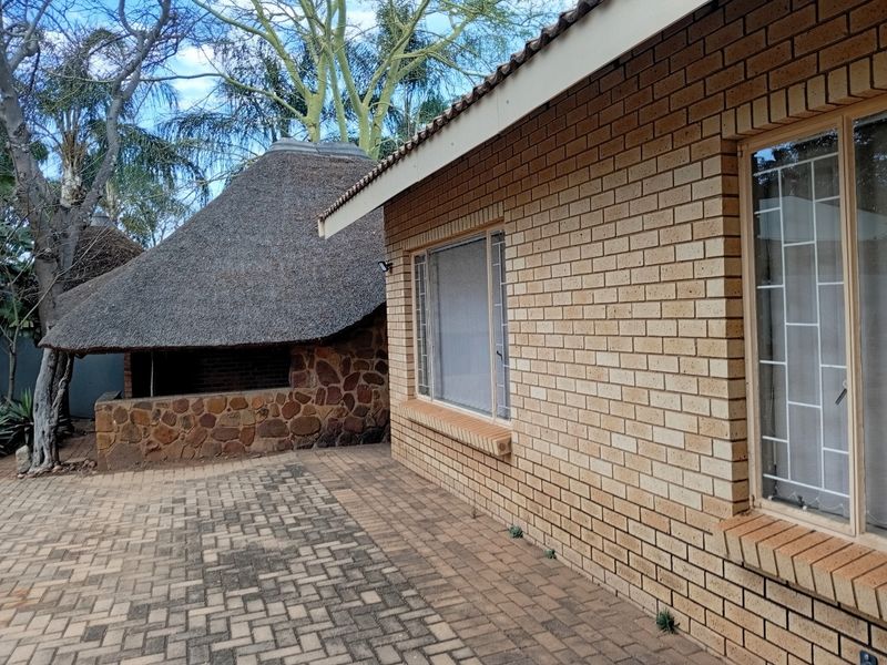 Rear exterior view featuring a face brick house facade, paved patio area, and a separate thatched roof lapa structure.