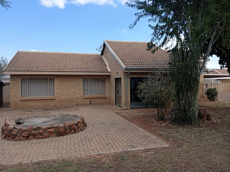 Rear view of a brick house featuring a paved patio area, a stone fire pit, and sliding glass door access to the interior.