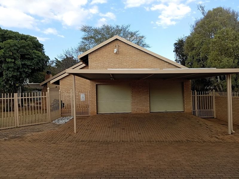 Front view of a facebrick house featuring a double garage with roll-up doors and an attached carport over a paved driveway.