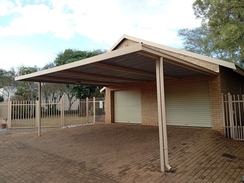 A double garage with roller shutter doors and an attached covered carport, featuring brick construction and a paved driveway.