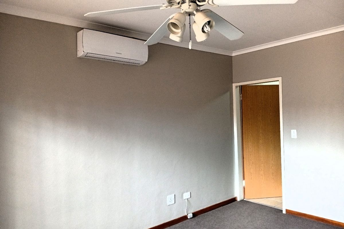 An empty bedroom featuring neutral wall paint, carpeted flooring, a ceiling fan, and a wall-mounted split-system air conditioning unit.