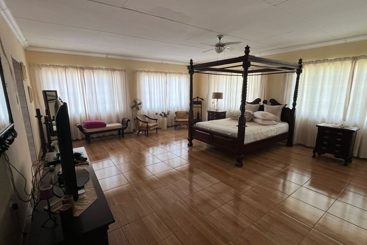 Spacious bedroom featuring tiled flooring, ceiling fan, and large windows with curtains, offering a neutral canvas for interior design updates.