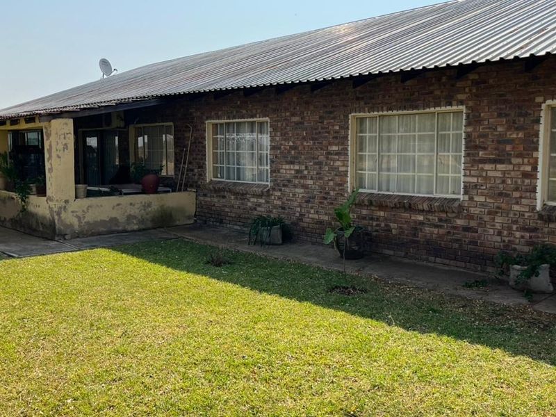 Rear view of a face brick small holding dwelling featuring a corrugated metal roof and a covered patio area overlooking the garden.