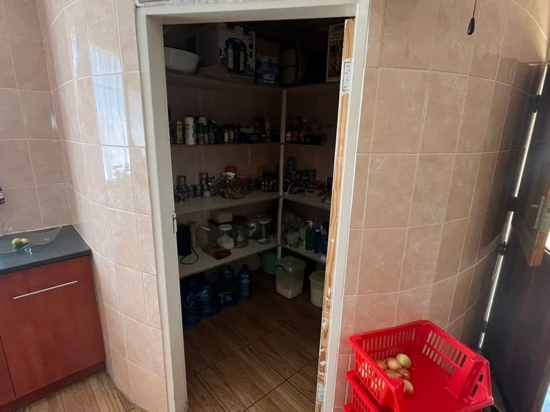 A functional scullery or pantry area featuring built-in shelving, tiled walls, and tiled flooring, providing convenient additional storage space adjacent to the kitchen.