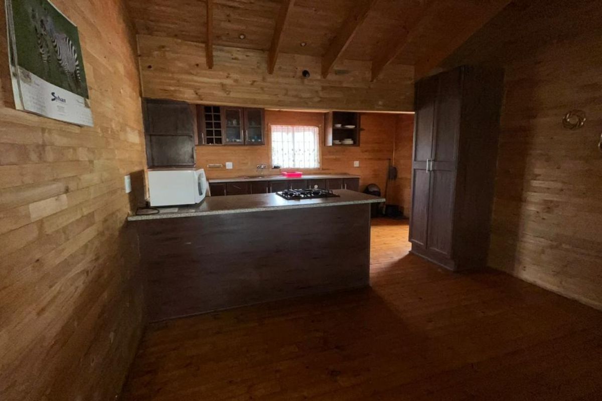 Rustic kitchen featuring timber wall cladding, exposed ceiling beams, a central island with a gas hob, and ample built-in cabinetry.