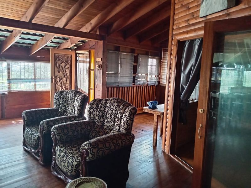 Rustic living area featuring exposed timber ceiling beams, wood-paneled walls, timber flooring, and sliding glass door access.