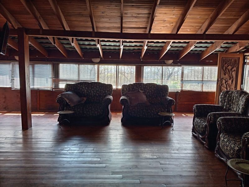 Spacious living area featuring rustic exposed timber ceiling beams, warm timber plank flooring, and extensive timber wall paneling with large windows.