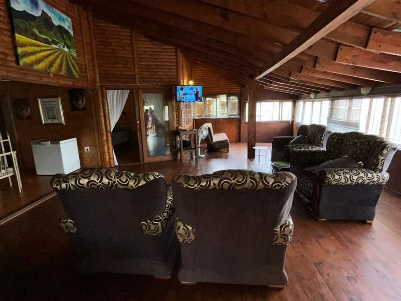 Spacious living area featuring rustic timber wall paneling, exposed wooden ceiling beams, and large windows providing ample natural light.