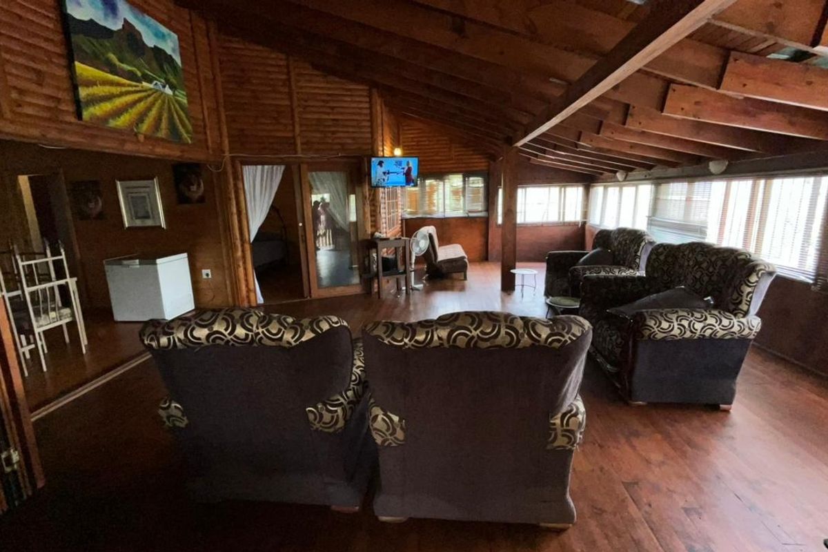 Spacious living area featuring rustic timber wall paneling, exposed wooden ceiling beams, and large windows providing ample natural light.