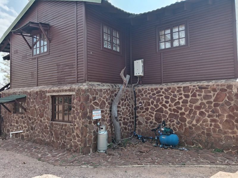 Rear exterior view of a timber and stone-clad house featuring an external gas geyser and water pump system.