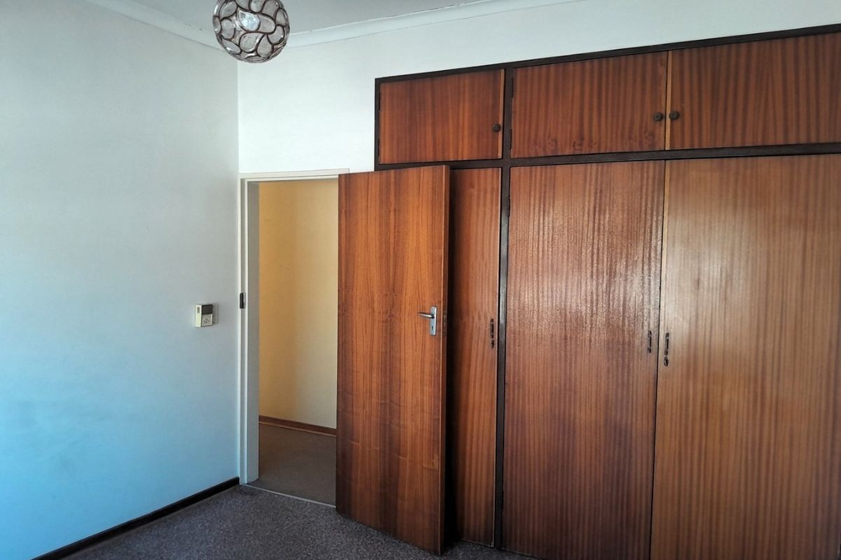 A bedroom featuring built-in wooden cupboards and carpeted flooring, offering a functional space ready for modernization.