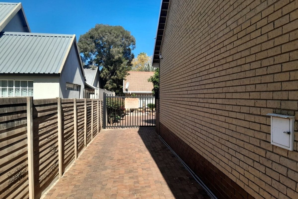 A side walkway featuring brick paving, a brick exterior wall, and a secure metal gate leading to the rear area of the townhouse.