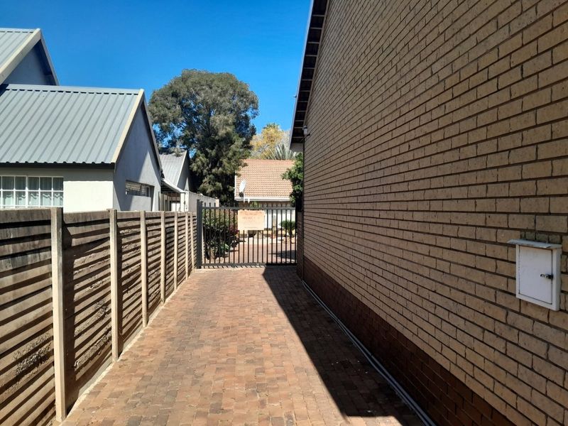 A side walkway featuring brick paving, a brick exterior wall, and a secure metal gate leading to the rear area of the townhouse.