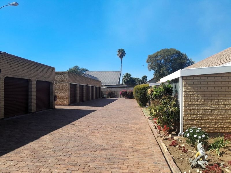 A view of the townhouse complex driveway featuring multiple garage units with face brick exteriors and neat brick paving.