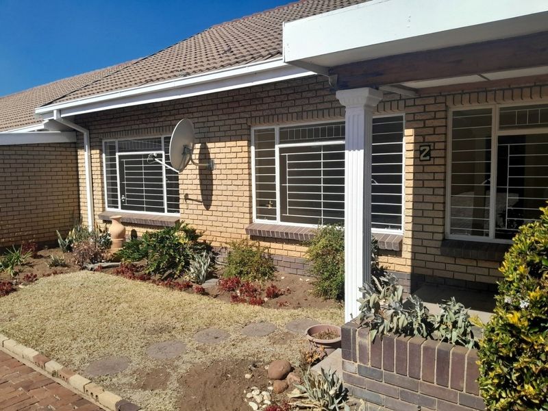 Front elevation of a brick townhouse featuring a covered porch, security bars on windows, and a small front garden area.