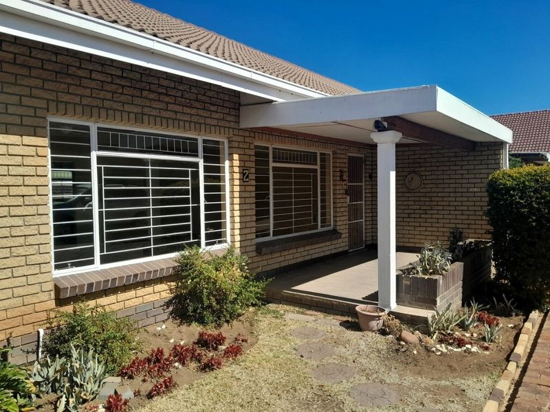 Front elevation of a face brick townhouse featuring a covered porch, security bars on windows, and a small landscaped garden area.