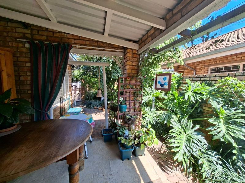 A covered brick patio area featuring paved flooring and direct access to a landscaped garden space, offering a private outdoor retreat.
