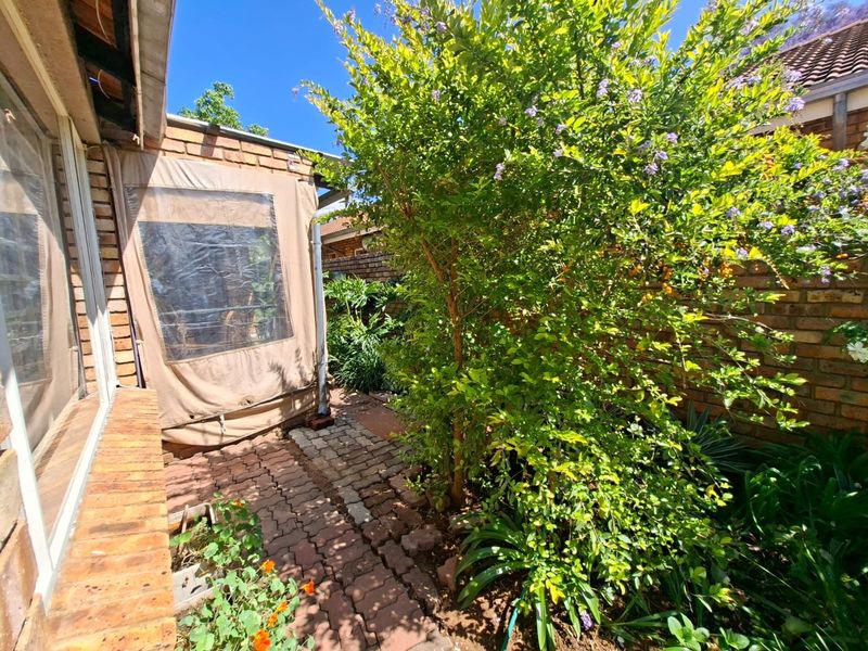 A rear courtyard area featuring brick paving, established garden greenery, and a canvas patio enclosure attached to the townhouse structure.