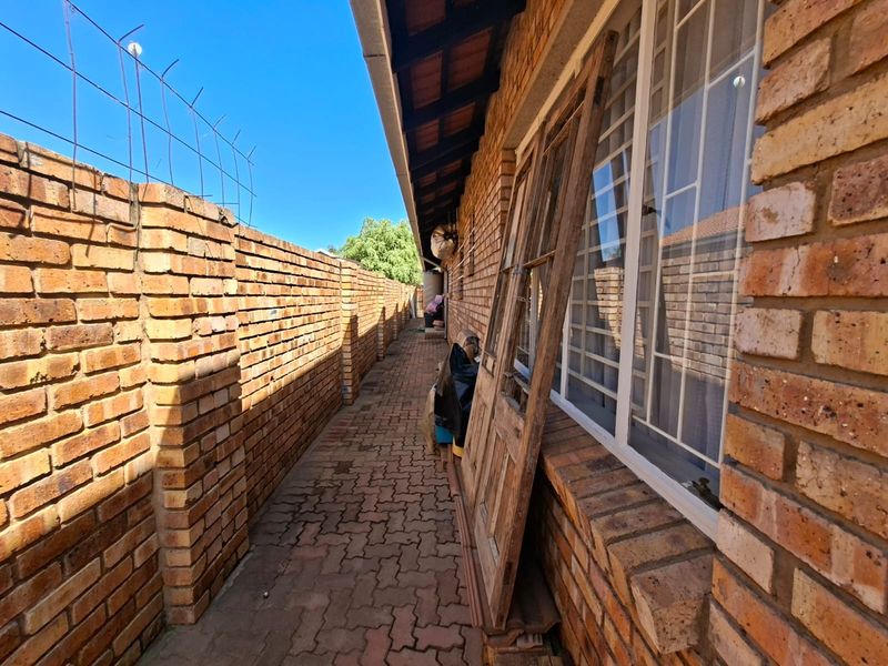 A narrow exterior side passage featuring brick boundary walls, paved flooring, and security window bars along the side of the townhouse.