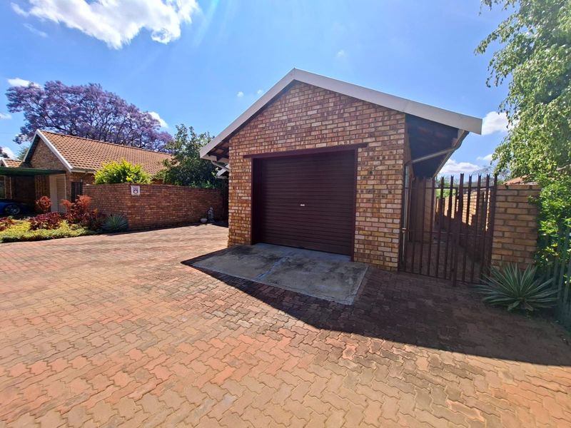 A detached brick garage with a roll-up door, situated on a paved driveway within a secure townhouse complex.