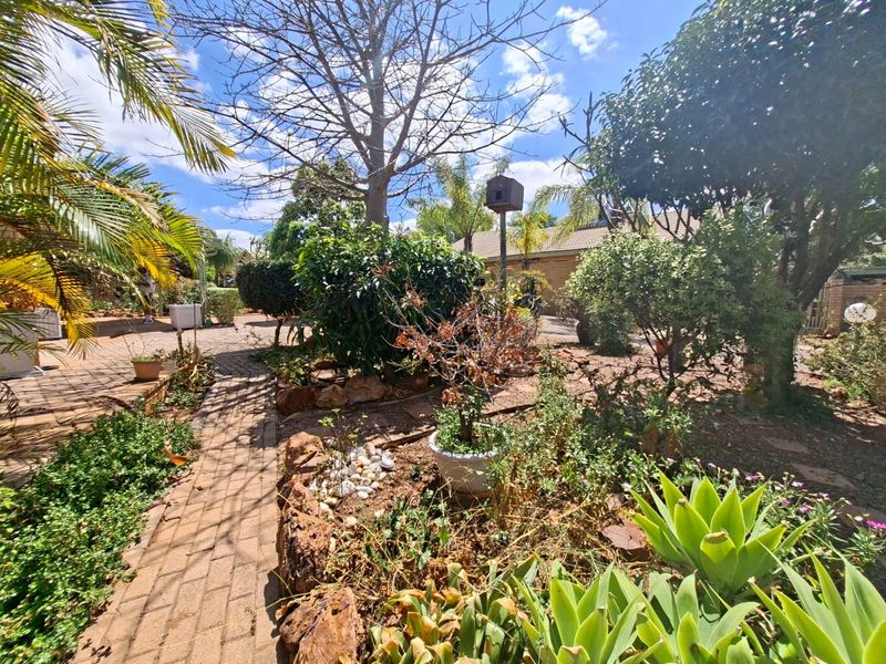 A landscaped garden area featuring a brick paved pathway, mature trees, and established garden beds with rock retaining borders.