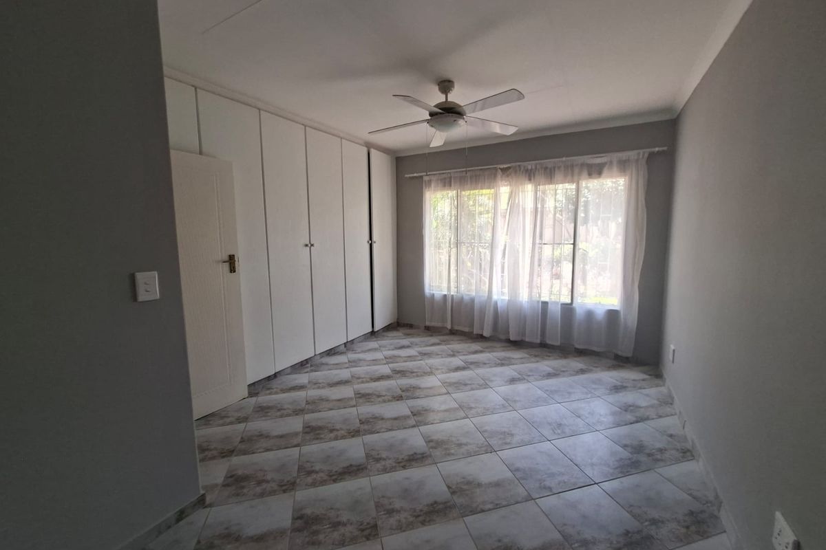 A bright, empty bedroom featuring neutral tiled flooring, built-in cupboards, and a ceiling fan, offering a clean canvas for personalization.