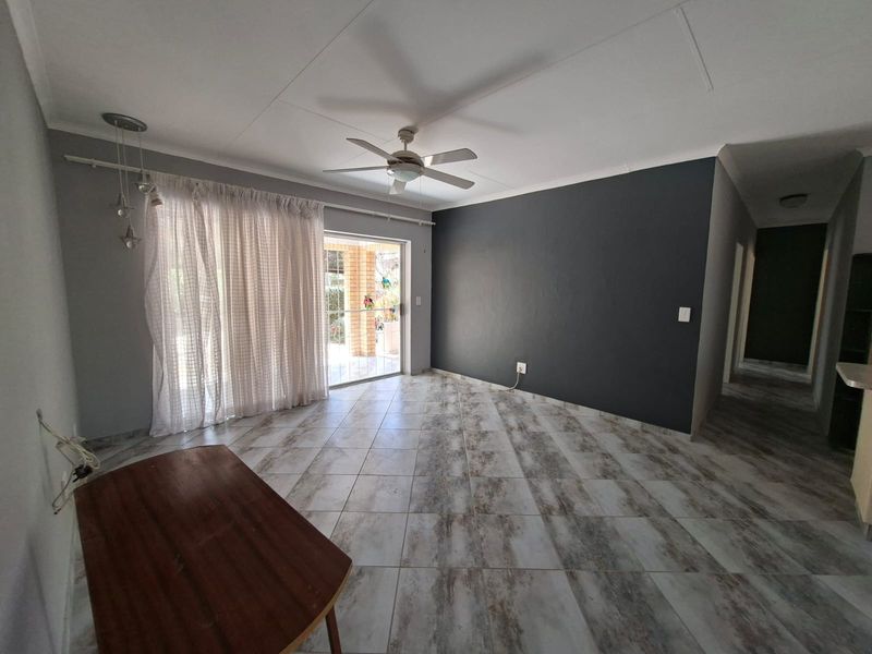 Spacious living area featuring neutral tiled flooring, a ceiling fan, and a sliding glass door providing access to the outdoor patio.