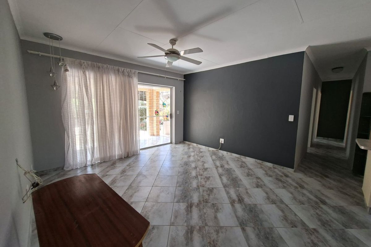 Spacious living area featuring neutral tiled flooring, a ceiling fan, and a sliding glass door providing access to the outdoor patio.