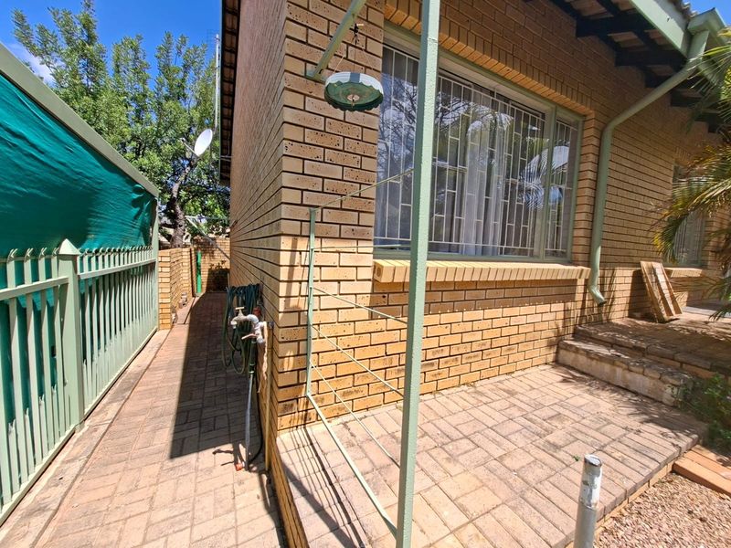A side view of the property featuring face brick exterior, paved patio area, security bars on windows, and metal fencing.