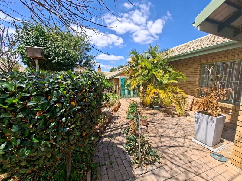 A rear exterior view of the property featuring a brick-paved walkway, face brick facade, and established garden area with security features.