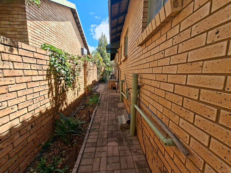 A narrow side passage featuring brick paving, face brick walls, and exposed external plumbing infrastructure.