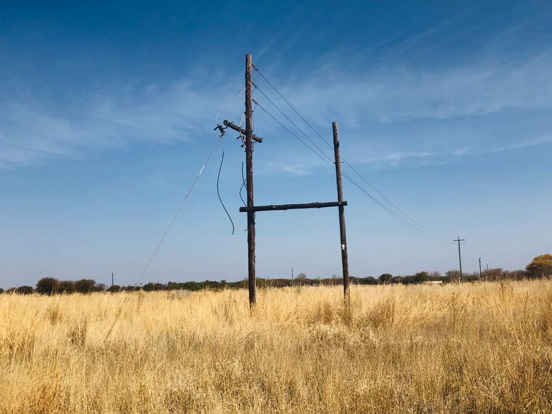 A view of a vacant residential plot featuring damaged utility poles and hanging power lines in an open field.