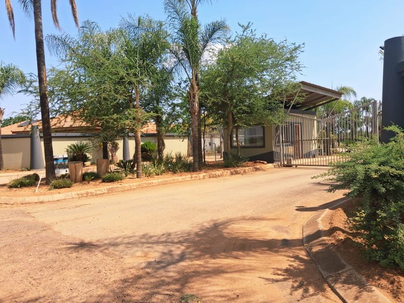 Front view of a residential property entrance featuring a secure gate, guard house, and well-maintained landscaped garden area.