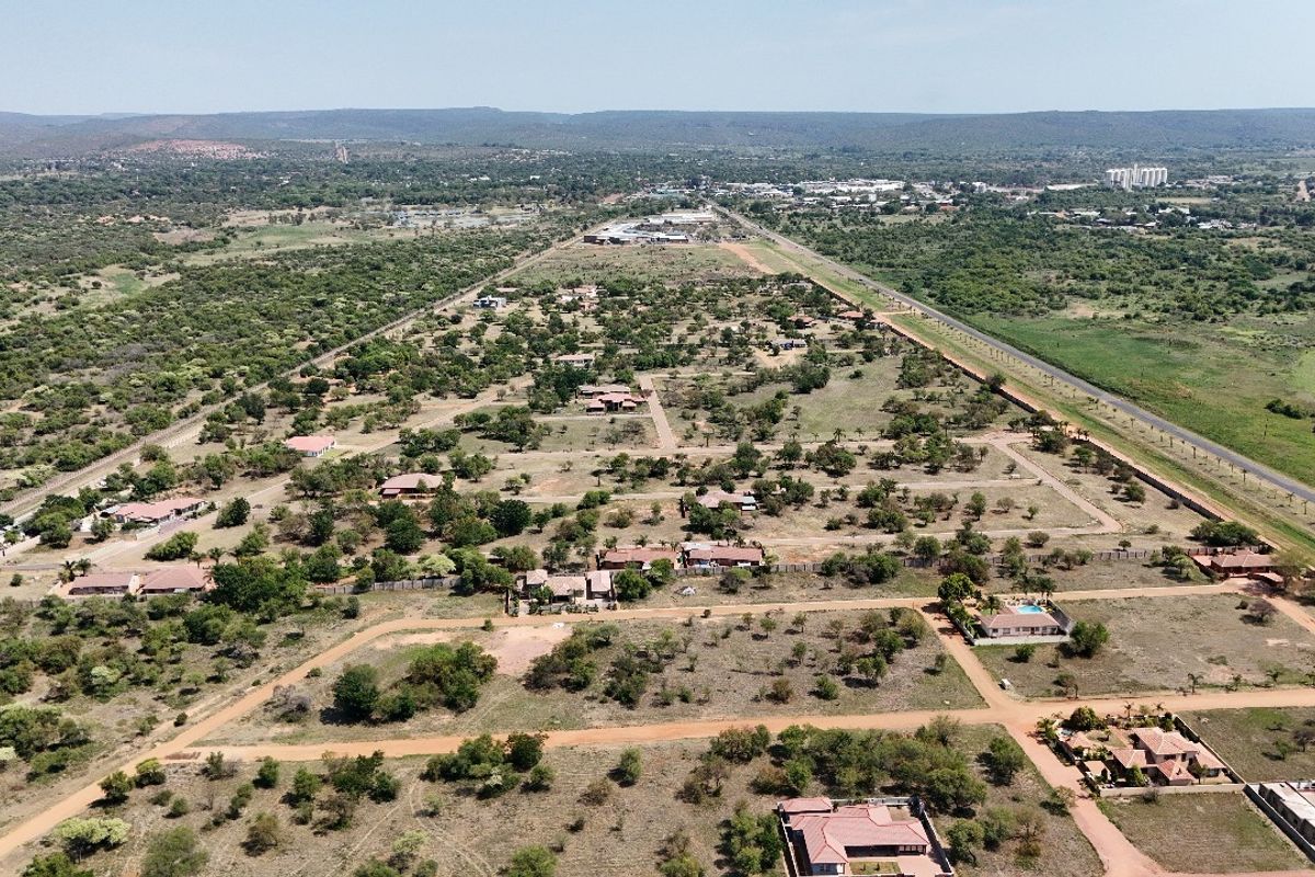 An aerial view of a residential estate featuring multiple plots, dirt road infrastructure, and scattered housing developments within a natural landscape.