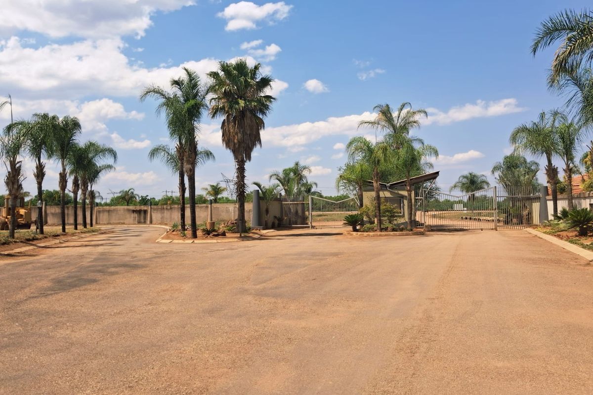 Front entrance view of the residential property featuring a secure gated access point, perimeter walling, and established palm trees.