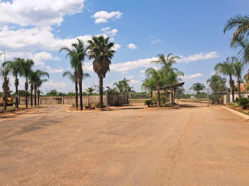 Front entrance view of the residential property featuring a secure gated access point, perimeter walling, and established palm trees.