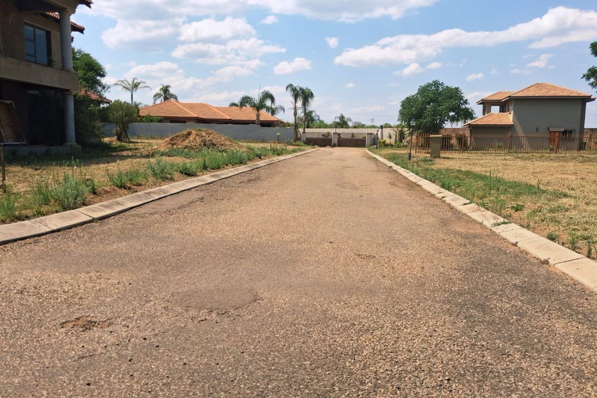 A view of a paved residential street with concrete curbing, showing surrounding properties and perimeter fencing in a suburban estate setting.