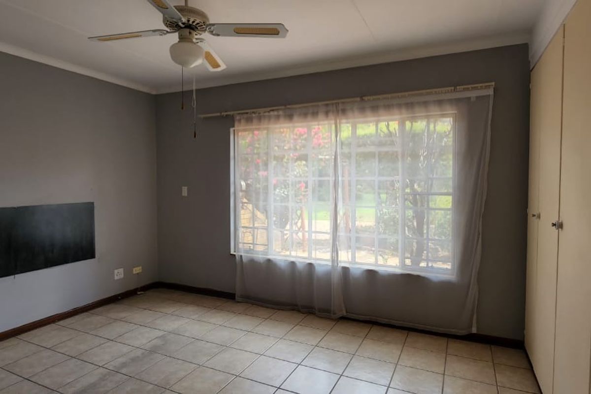 A spacious, empty bedroom featuring tiled flooring, a ceiling fan, and built-in cupboards, offering a neutral canvas for potential updates.
