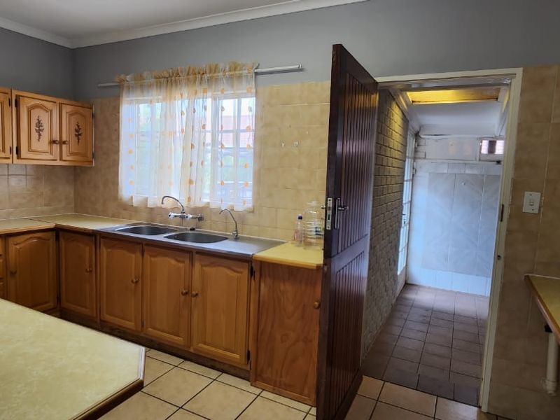 A functional kitchen featuring wooden cabinetry, laminate countertops, a double basin sink, and tiled splashbacks, with an adjacent utility area.