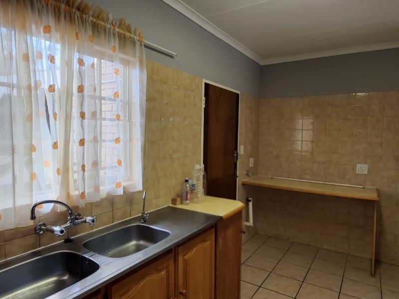 A functional kitchen area featuring a double basin stainless steel sink, tiled splashbacks, and built-in cabinetry with laminate countertops.