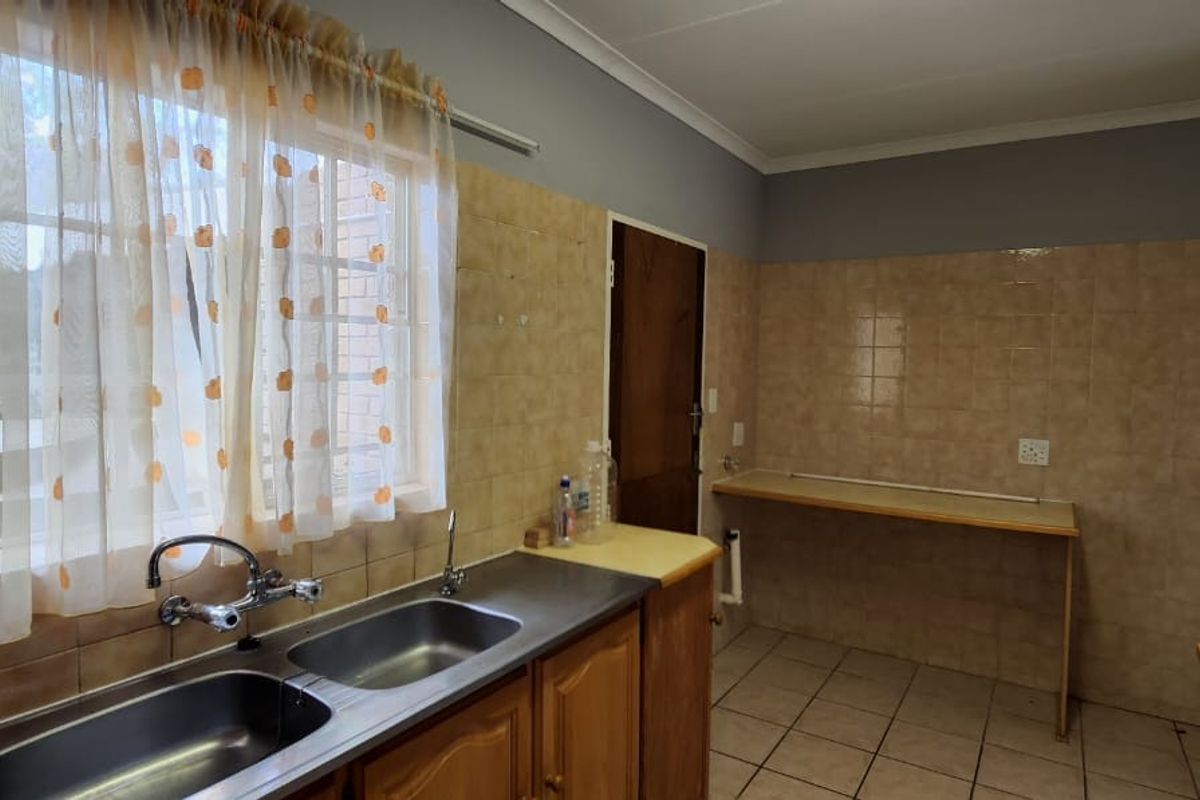 A functional kitchen area featuring a double basin stainless steel sink, tiled splashbacks, and built-in cabinetry with laminate countertops.