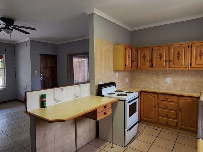 Open plan kitchen and living area featuring tiled floors, wooden cabinetry, a breakfast counter, and a ceiling fan in a functional, dated layout.