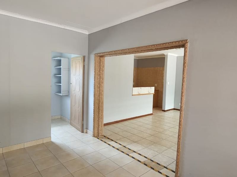 An empty living area featuring neutral grey walls, ceramic floor tiles, and an open archway leading to an adjacent room with built-in shelving.