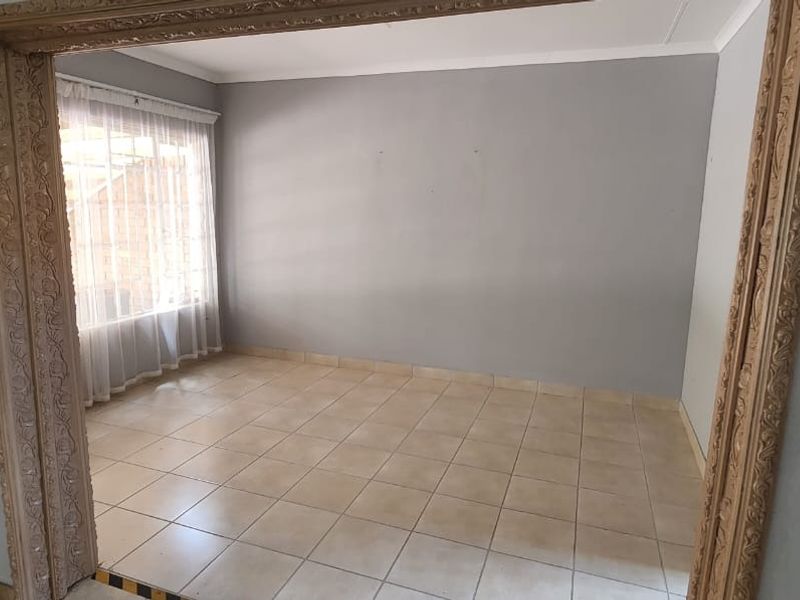 An empty living room featuring neutral grey walls, tiled flooring, and a decorative ornate door frame leading into the space.