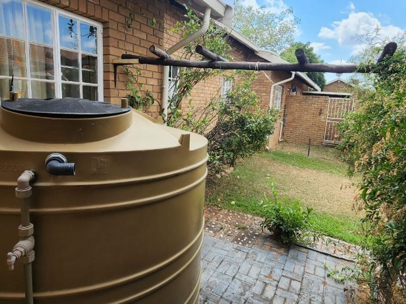 Rear exterior view of the townhouse featuring a brick facade, paved patio area, and a large water storage tank.
