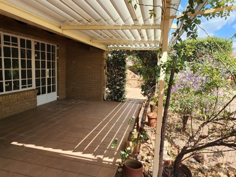 A covered outdoor patio area featuring tiled flooring, brick walls, and a louvred roof, providing a functional space for outdoor relaxation.