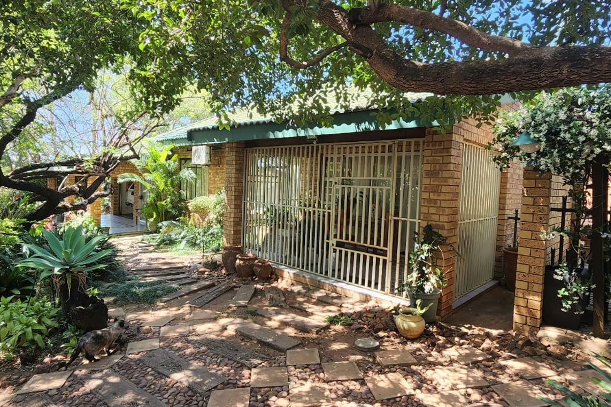 A view of the rear exterior featuring a face brick facade, secure metal gates, and a landscaped garden with a paved walkway.