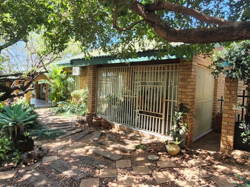 A view of the rear exterior featuring a face brick facade, secure metal gates, and a landscaped garden with a paved walkway.